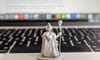 Photo showing a figurine of a wizard, holding a staff, gazing over a Macbook keyboard. In the distance, a document rises up