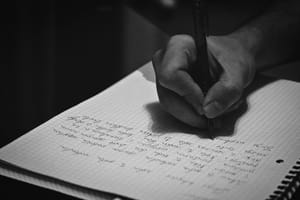 Black-and-white photo of a hand holding a pen, writing on a page of graph paper